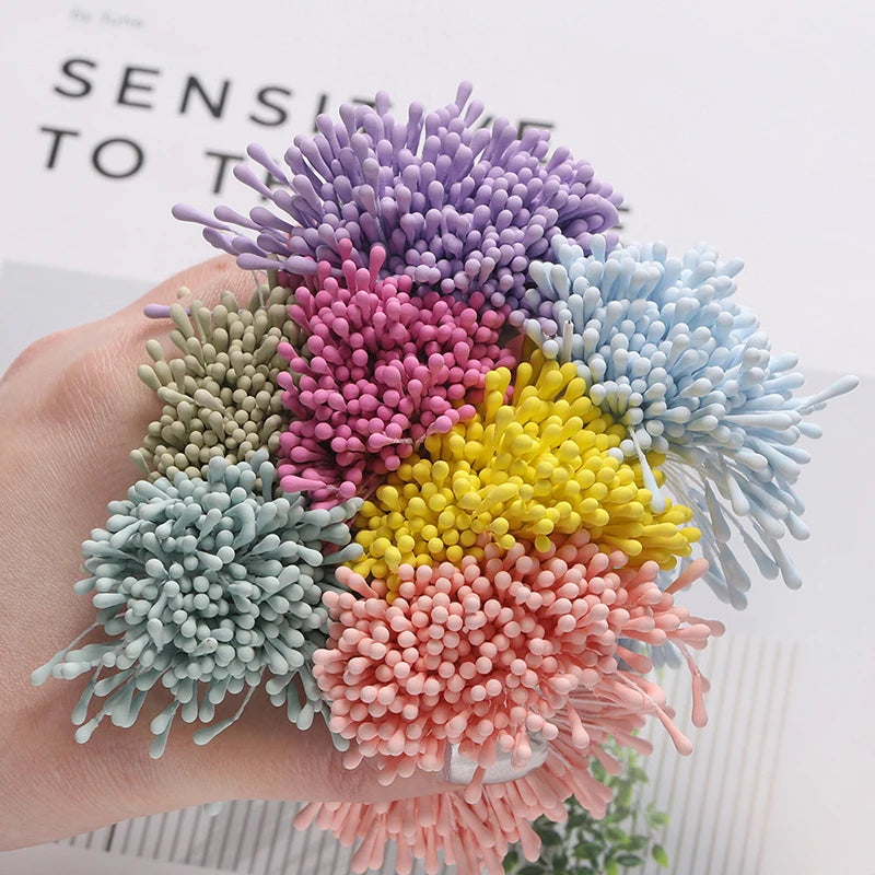 A hand holds a cluster of 400 pearl flower stamens in various shades of purple, pink, and blue for DIY crafts.