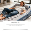 A man relaxing on a gray inflatable mattress indoors with an inflatable repair kit nearby.