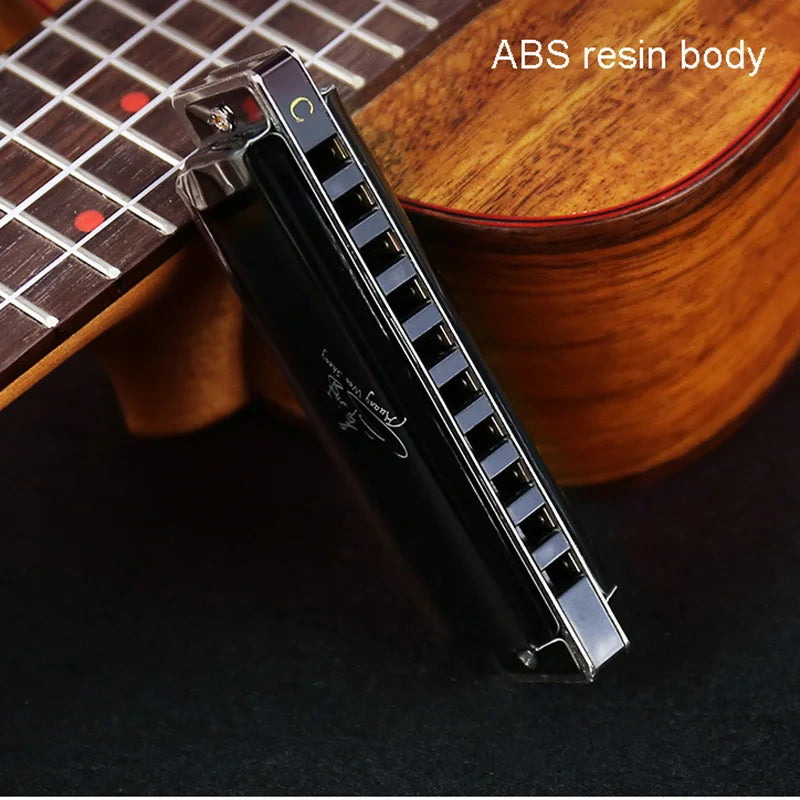 Black ABS resin harmonica with a case resting on a wooden guitar body.