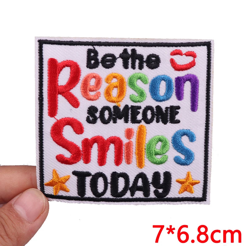 A square embroidered patch featuring colorful letters spelling out Be the Reason Someone Smiles Today