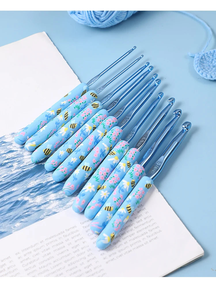 A set of blue ergonomic crochet hooks featuring a bee design, arranged diagonally on a white background.