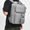 A person is carrying a gray cement ash travel backpack with a laptop compartment.