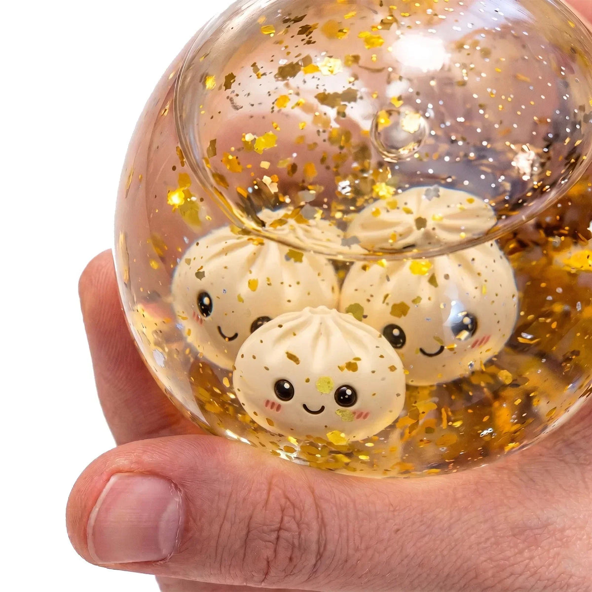 A hand holds a clear glass orb filled with golden liquid and several white squishy dumpling fidget toys.