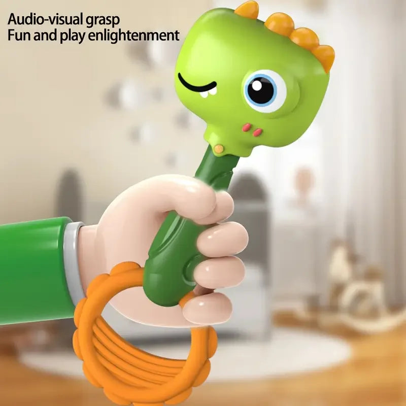 A hand is grasping a green cartoon animal rattle toy with a yellow ring, demonstrating audio-visual grasp fun.