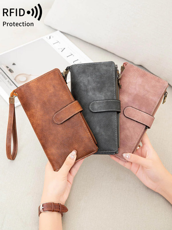 A hand holds a brown leather wallet with a wristlet strap and a gray wallet, demonstrating RFID protection.
