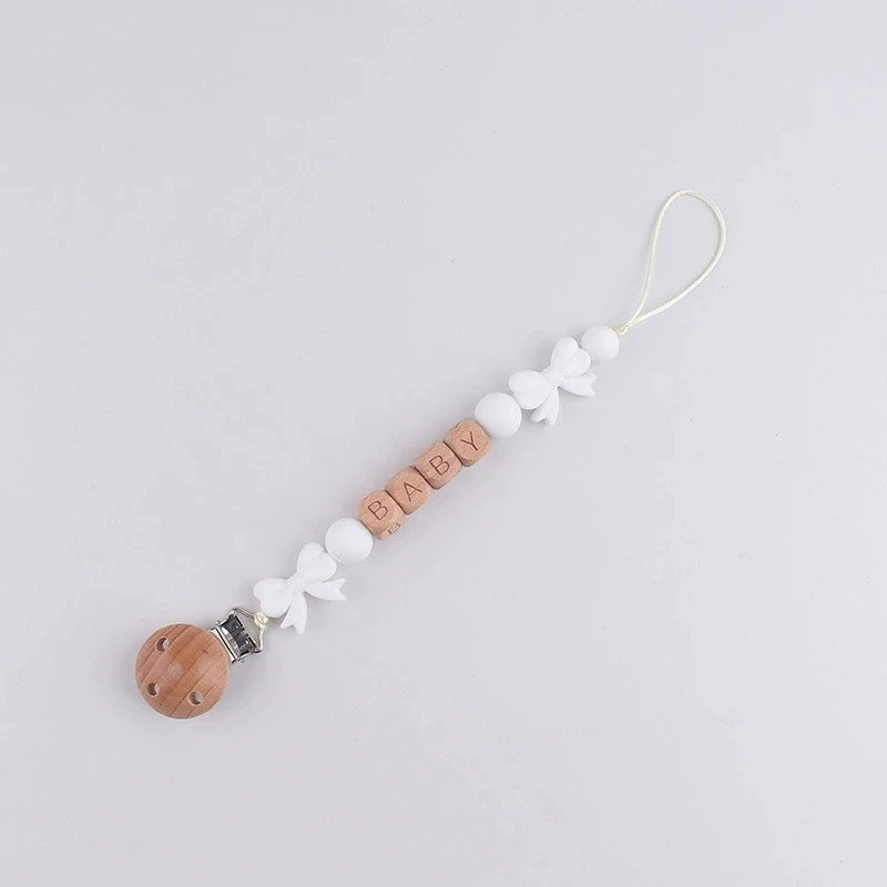 A brown silicone pacifier clip with a white floral design and a gold lanyard attached.