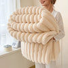 A woman holds a large, fluffy, beige flannel blanket with a coiled texture.