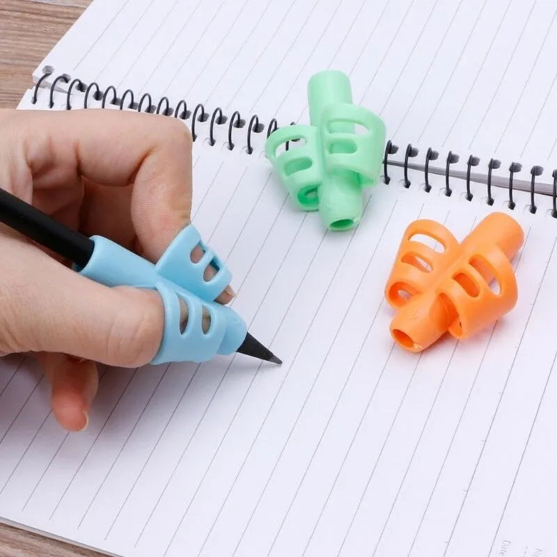 An ergonomic pencil grip trainer set featuring green and orange silicone grips placed on a lined notepad next to a blue penci