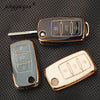 Three TPU silicone car key cases in gold and silver tones are displayed on a dark surface.