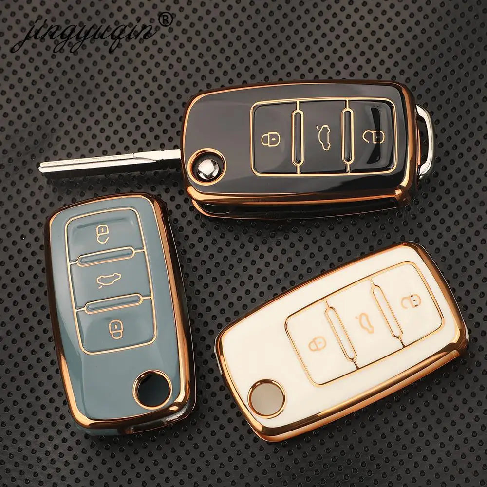 Three TPU silicone car key cases in gold and silver tones are displayed on a dark surface.