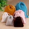 A collection of velvet drawstring jewelry pouches in shades of orange, pink, beige, gray, and blue resting on a woven surface