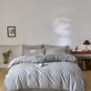 A light gray quilted duvet cover set with matching pillowcases on a bed in a bright room.