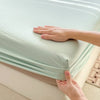 A hand is holding a light mint green fitted sheet, showing the elastic band and fabric texture.