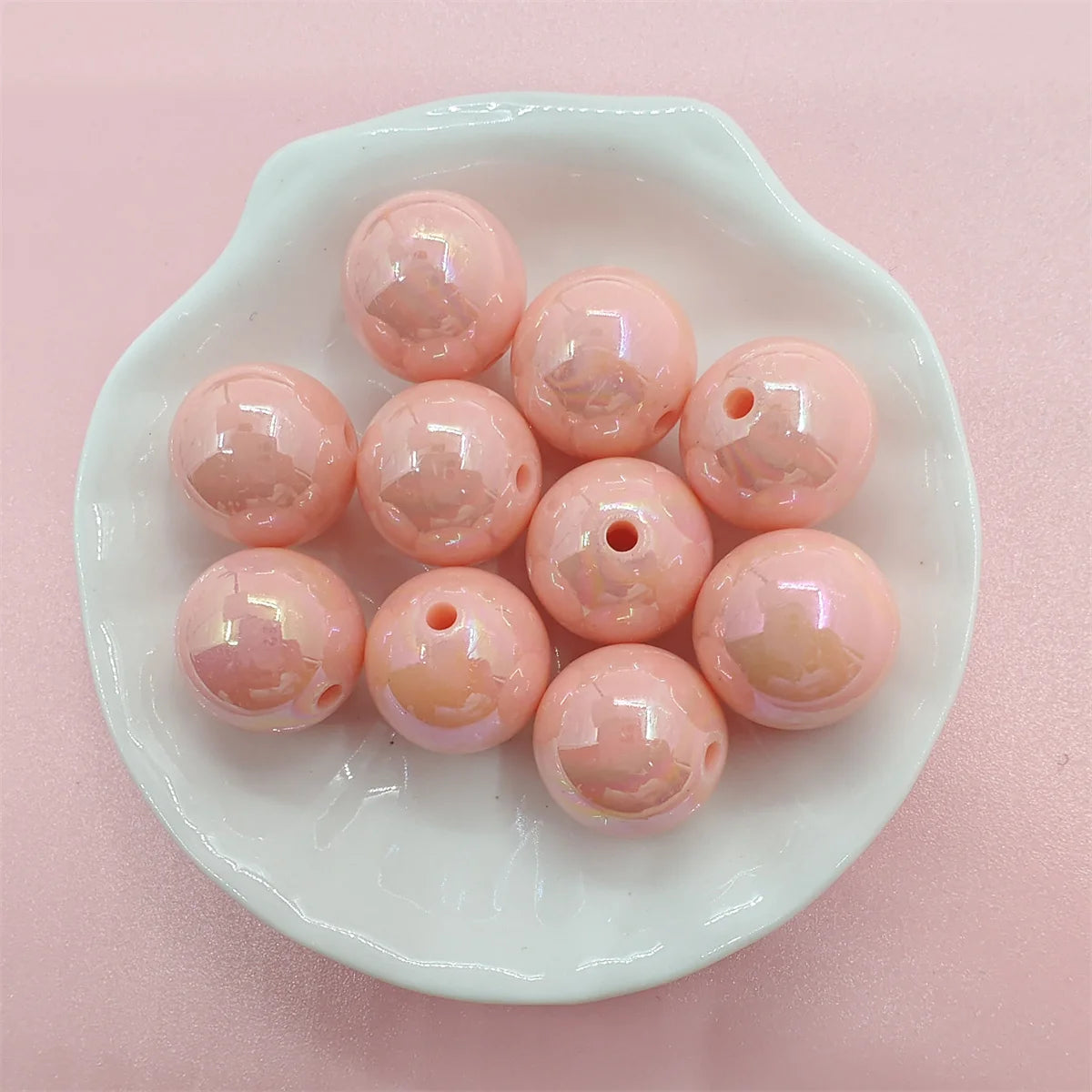 A white dish holds several pink and iridescent acrylic beads for jewelry making.