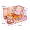 A pink wooden dollhouse miniature building kit featuring furniture and a bedroom setup.