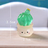A bright green succulent cactus miniature with a yellow top is planted in a small, translucent white pot.