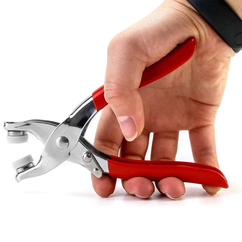 A hand is holding a red and silver snap fastener kit with hand press pliers.