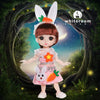 A pink fashion doll with white ears and orange accents stands in a natural, leafy setting.