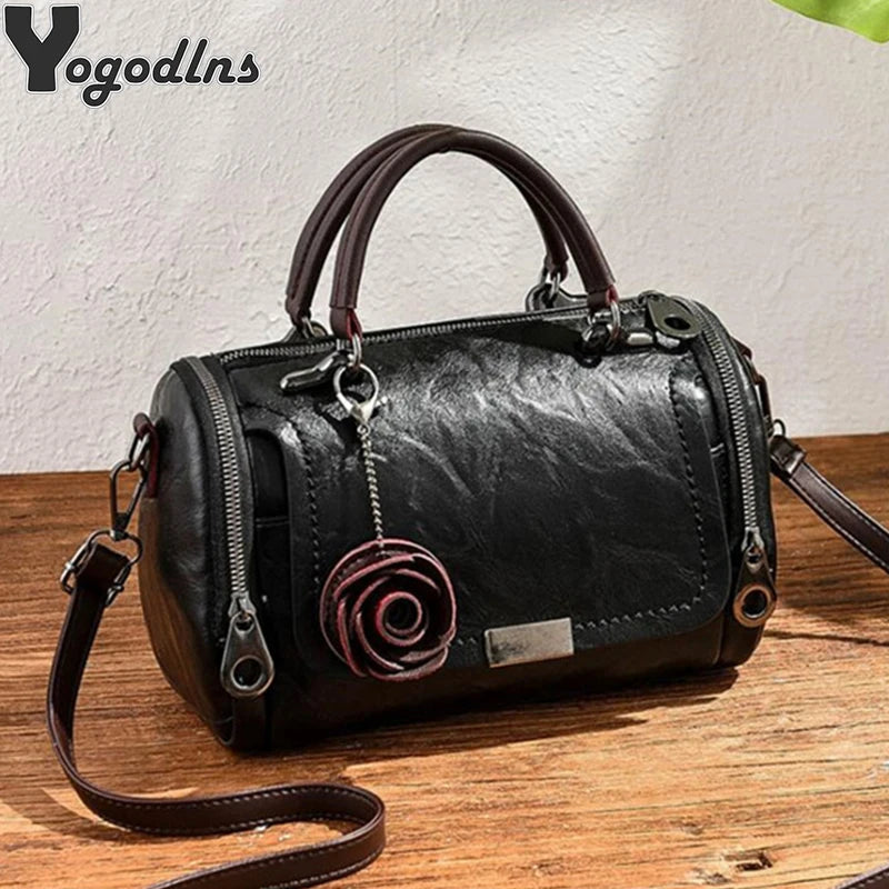 A black leather crossbody bag with a rose pendant and brown leather strap resting on a wooden surface.