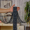 A hand is pulling a black crystal beaded string curtain across a window or doorway.