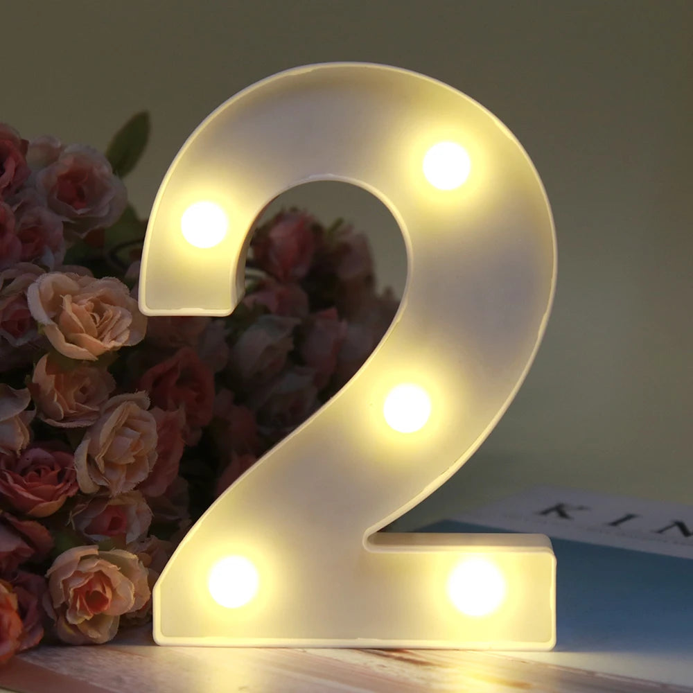 Lumière de nuit alphabet LED blanche brillante en forme de 2, posée sur une surface en bois à côté de roses.