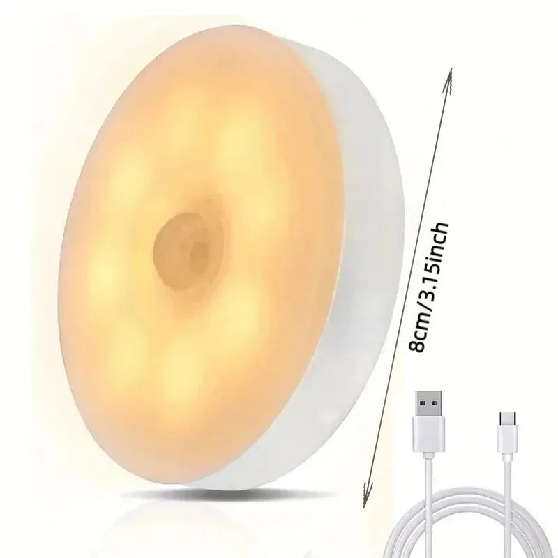 A round, white LED night light with a translucent yellow glow and a USB charging cable is shown.