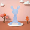 A light blue silicone cartoon rabbit teether displayed against a pink wall with white clouds and an orange tree.