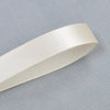 A roll of double face satin ribbon in a light cream color, shown diagonally against a gray patterned background.
