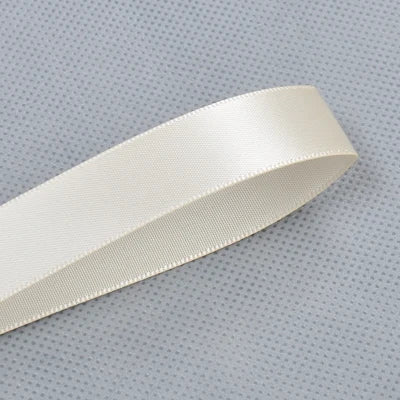 A roll of double face satin ribbon in a light cream color, shown diagonally against a gray patterned background.