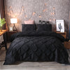 A black quilted comforter and pillows displayed on a bed with string lights in a bedroom setting.