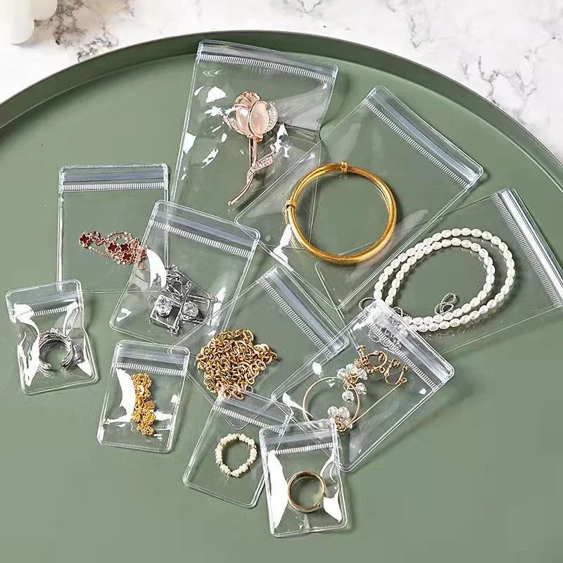Clear self-sealing jewelry storage bags filled with various gold and silver rings, necklaces, and earrings on a green tray