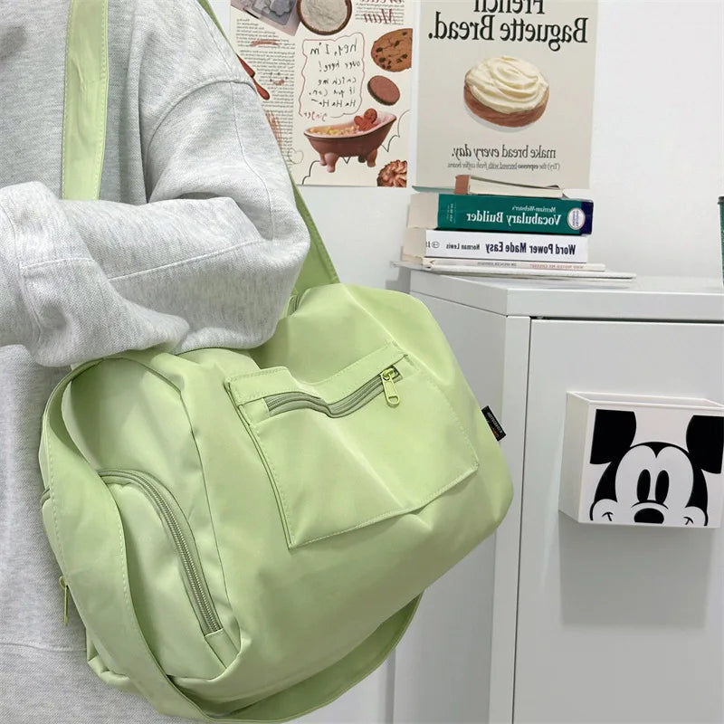 A light green canvas travel tote bag with a strap is shown next to a gray hoodie and some printed materials.