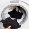 Une main tient une éponge pour retirer les poils d'un ours en peluche noir dans un récipient blanc.