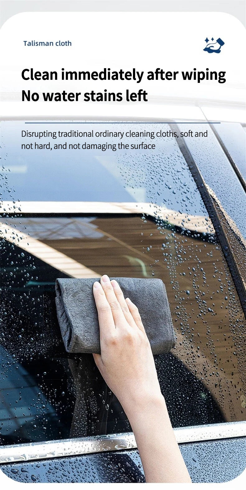 A hand wipes water stains from a car window using a dark gray microfiber cloth.
