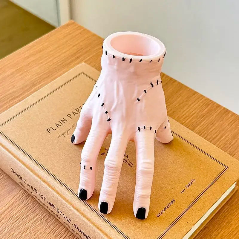 A pink resin Halloween hand planter and pen holder resting on a brown book.