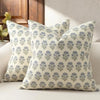 A close-up of a beige throw pillow cover with a blue floral pattern resting on a light sofa.