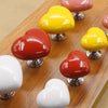 A collection of heart-shaped toilet flush buttons in yellow, red, and white displayed on a wooden surface.