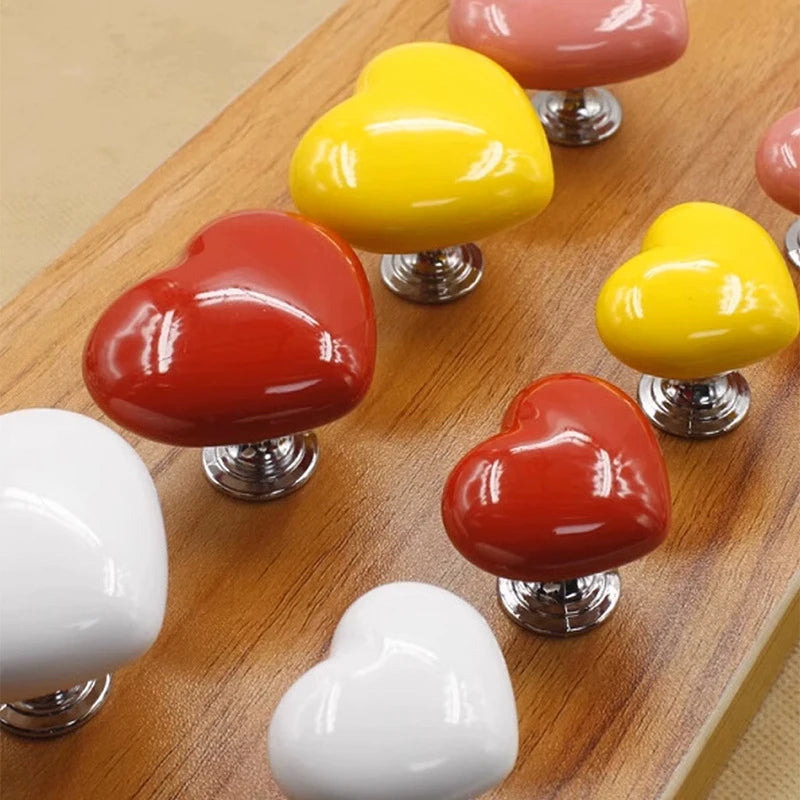 A collection of heart-shaped toilet flush buttons in yellow, red, and white displayed on a wooden surface.