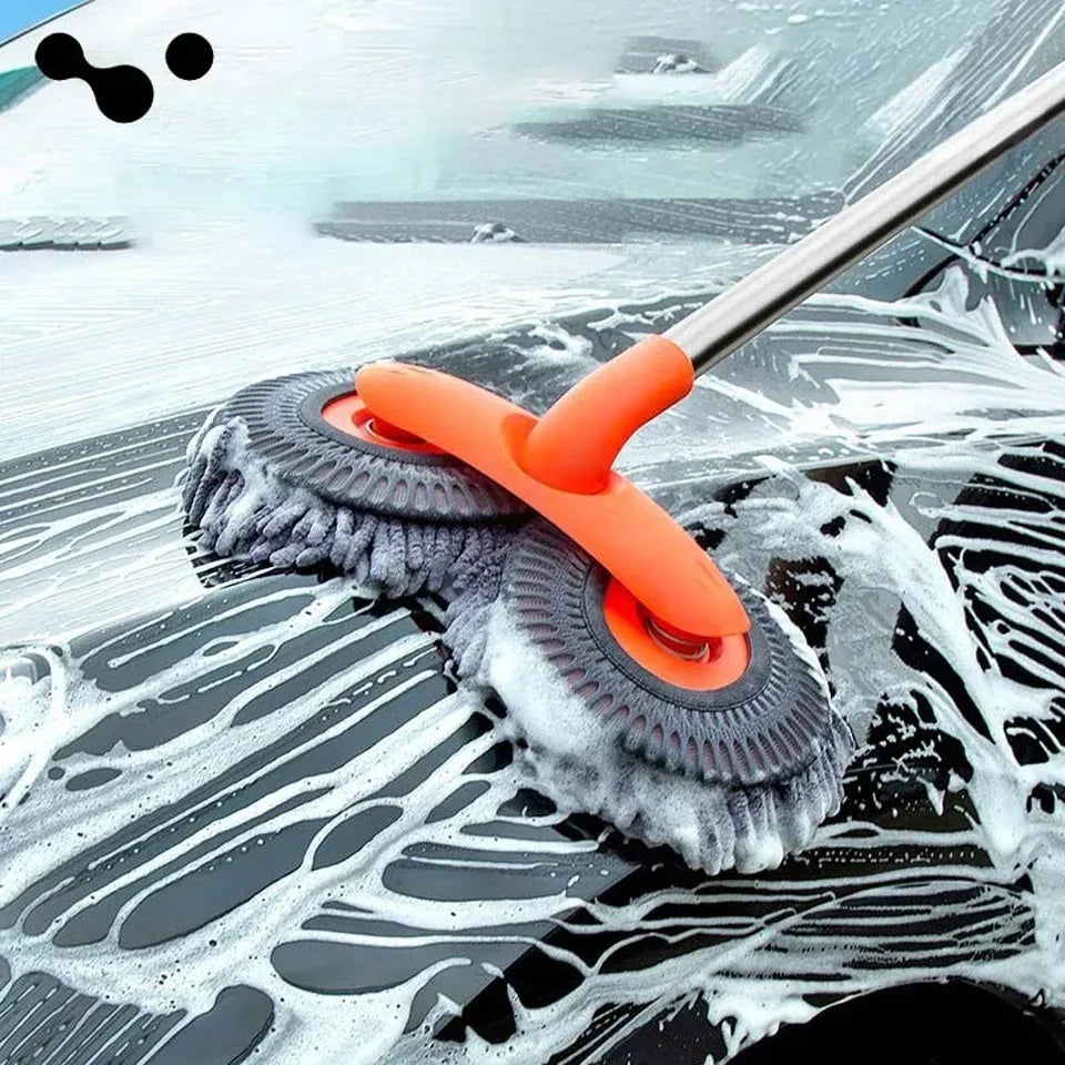 An orange extendable car wash mop with a dual chenille brush head cleaning water spots on a dark car surface.
