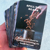 A hand holds a deck of Spill the Beans oracle cards featuring a dark background and text about revealing everything.