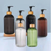 A set of four refillable soap dispensers in various glass and black bottles with wooden tops.