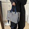 A person holds a striped canvas tote bag with dark blue straps and inner pockets against a white background.