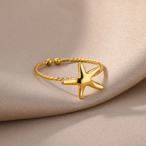 Bague en acier inoxydable plaqué or avec motif étoile, posée sur un tissu beige.