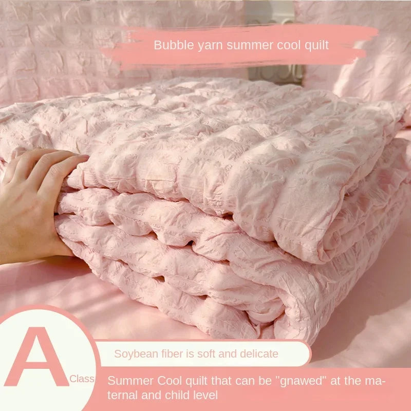 Pink bubble yarn summer cool quilt shown being folded on a bed with a hand