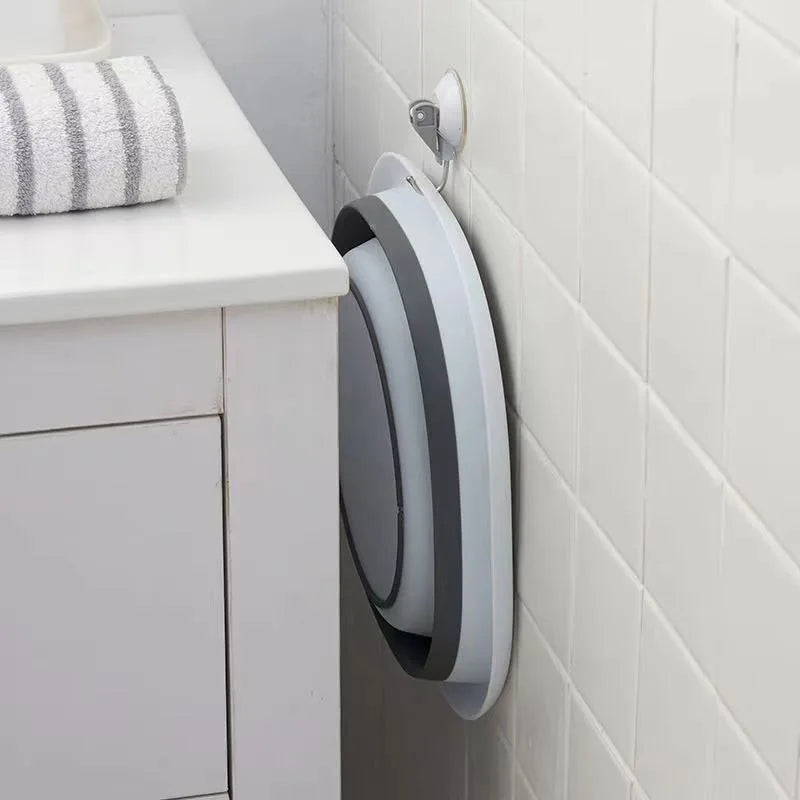A silver and gray collapsible silicone washbasin hanging on a white tiled wall.