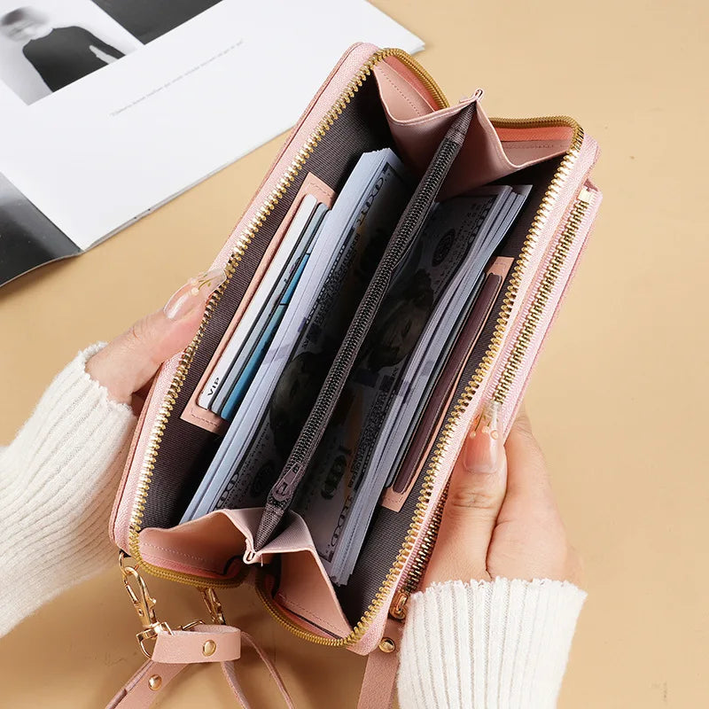 A hand holds a pink leather crossbody phone bag with a gold zipper, showing card slots inside.