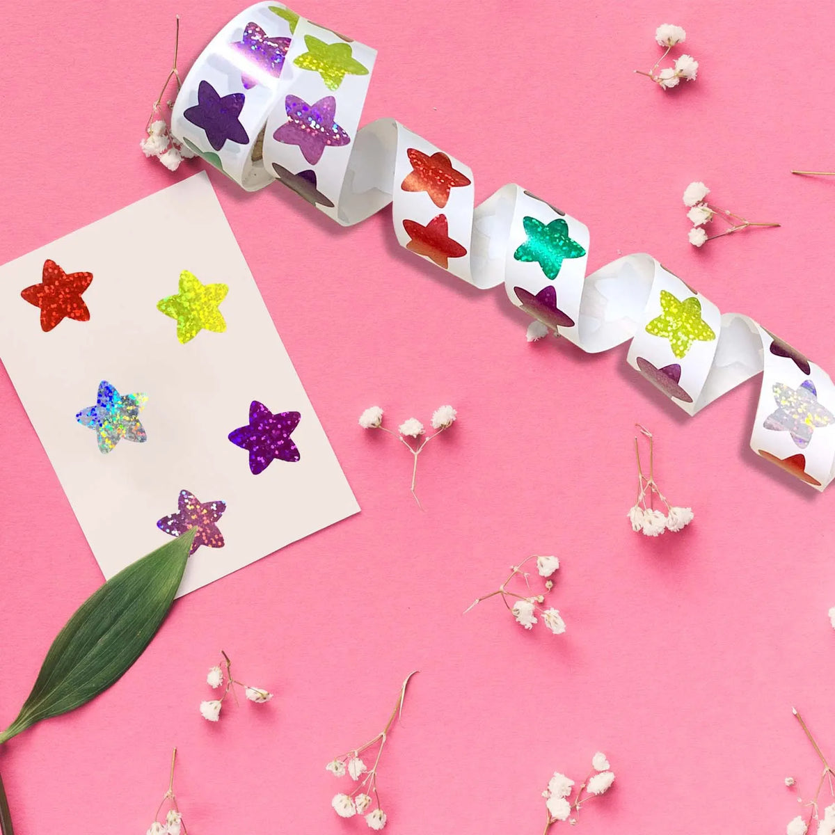 A roll of 500 glitter star stickers in various colors is displayed on a pink background.