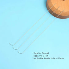 Three curved stainless steel beading needles laid diagonally on a light blue surface.