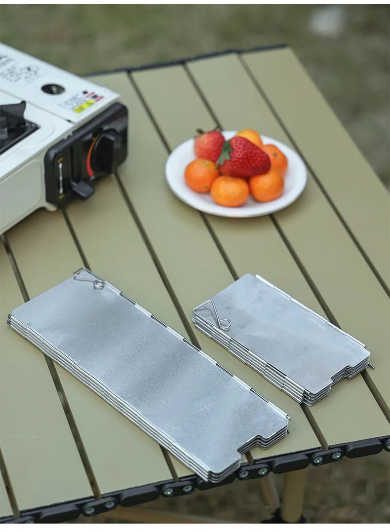 A silver portable aluminum alloy windshield is placed on a wooden table next to some fresh fruit.
