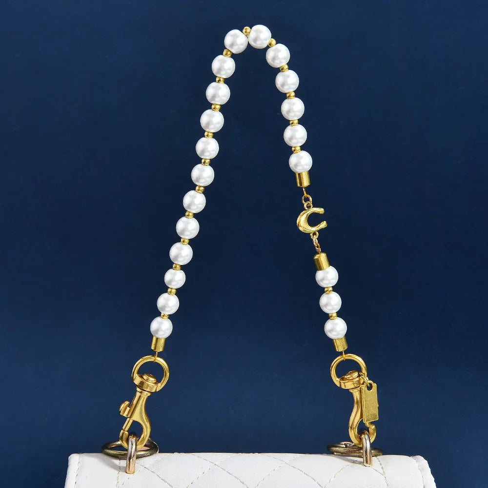 A gold-toned pearl necklace with a letter C charm displayed on a white quilted purse.